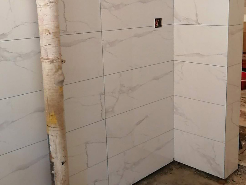 衛(wèi)生間瓷磚鋪貼：基層處理：首先應(yīng)除去基層表面的污垢，油漬，浮灰;除去基層上所有涂料層，膩子層;如果基層未能達(dá)到平整度要求，需對基層進(jìn)行預(yù)先的找平處理。  放樣：鋪貼瓷磚前需事先找好垂直線，以此為基準(zhǔn)鋪貼的瓷磚高低均勻、垂直美觀;此外，施工前在墻體四周需彈出標(biāo)高控制線，在地面彈出十字線，以控制地磚分隔尺寸。  預(yù)鋪：首先應(yīng)對瓷磚的色彩、紋理、表面平整等進(jìn)行嚴(yán)格的挑選，然后按照圖紙要求預(yù)鋪。 調(diào)制粘結(jié)劑：加水后將粘結(jié)劑漿料攪拌至潤滑均勻，無明顯塊狀或糊狀結(jié)塊，攪拌后的漿料靜置5-10分鐘后再稍加攪拌1-2分鐘即可使用。在開始鋪貼施工前，需要先清理瓷磚表面的浮灰，污垢等。  抹漿料：將調(diào)制好的漿料均勻地抹在瓷磚背面，要求漿料飽滿。將瓷磚平整地鋪貼在基層上，使用橡膠錘將瓷磚拍實鋪平。施工過程中，可小幅度轉(zhuǎn)動瓷磚，使?jié){料與瓷磚背面充分接觸。 瓷磚鋪貼結(jié)束后24小時，可進(jìn)行嵌縫施工。將調(diào)制好的嵌縫劑均勻地涂在磚與磚的縫隙內(nèi)。嵌縫后用浸濕的織物清理多余的嵌縫劑，保持瓷磚表面清潔。