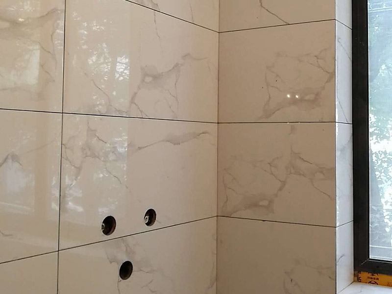 衛(wèi)生間瓷磚鋪貼：基層處理：首先應(yīng)除去基層表面的污垢，油漬，浮灰;除去基層上所有涂料層，膩子層;如果基層未能達(dá)到平整度要求，需對基層進(jìn)行預(yù)先的找平處理。  放樣：鋪貼瓷磚前需事先找好垂直線，以此為基準(zhǔn)鋪貼的瓷磚高低均勻、垂直美觀;此外，施工前在墻體四周需彈出標(biāo)高控制線，在地面彈出十字線，以控制地磚分隔尺寸。  預(yù)鋪：首先應(yīng)對瓷磚的色彩、紋理、表面平整等進(jìn)行嚴(yán)格的挑選，然后按照圖紙要求預(yù)鋪。 調(diào)制粘結(jié)劑：加水后將粘結(jié)劑漿料攪拌至潤滑均勻，無明顯塊狀或糊狀結(jié)塊，攪拌后的漿料靜置5-10分鐘后再稍加攪拌1-2分鐘即可使用。在開始鋪貼施工前，需要先清理瓷磚表面的浮灰，污垢等。  抹漿料：將調(diào)制好的漿料均勻地抹在瓷磚背面，要求漿料飽滿。將瓷磚平整地鋪貼在基層上，使用橡膠錘將瓷磚拍實鋪平。施工過程中，可小幅度轉(zhuǎn)動瓷磚，使?jié){料與瓷磚背面充分接觸。 瓷磚鋪貼結(jié)束后24小時，可進(jìn)行嵌縫施工。將調(diào)制好的嵌縫劑均勻地涂在磚與磚的縫隙內(nèi)。嵌縫后用浸濕的織物清理多余的嵌縫劑，保持瓷磚表面清潔。