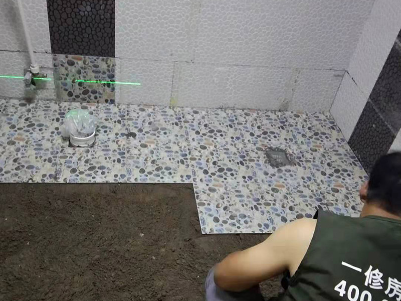 衛(wèi)生間地面花磚鋪貼:找平，就是在鋪仿古磚前，對(duì)鋪貼物表面進(jìn)行處理，如地面、內(nèi)墻面、外墻面等，消除表面附著的污物，并灑水進(jìn)行滋潤(rùn)，然后用水泥沙混合找平，通常使用灰鏟在表面不停的涂抹使水泥地面保持大致水平，一定要等到水泥沙混合物完全干爽后再行鋪貼。用一段較長(zhǎng)的細(xì)線，根據(jù)確定的鋪貼方式，在線上涂上顏色或白灰，然后在找平的地面上畫(huà)出仿古磚的位置及磚縫的參考線。 將亞光磚置入清水中浸泡，使瓷磚充分吸收水分，以不冒出氣泡為準(zhǔn)，防止干燥瓷磚在裝修完成后再次吸水而導(dǎo)致磚體變形。取出浸泡好的瓷磚，抹干水漬，在找平層上噴灑足夠的水，然后在磚背面均勻抹上水泥沙漿，沙漿厚度5~6cm為宜，鋪貼大規(guī)格亞光磚時(shí)適當(dāng)加厚；隨即將磚貼上，用木錘輕輕拍牢平整，避免空鼓，并隨時(shí)用直尺找平。