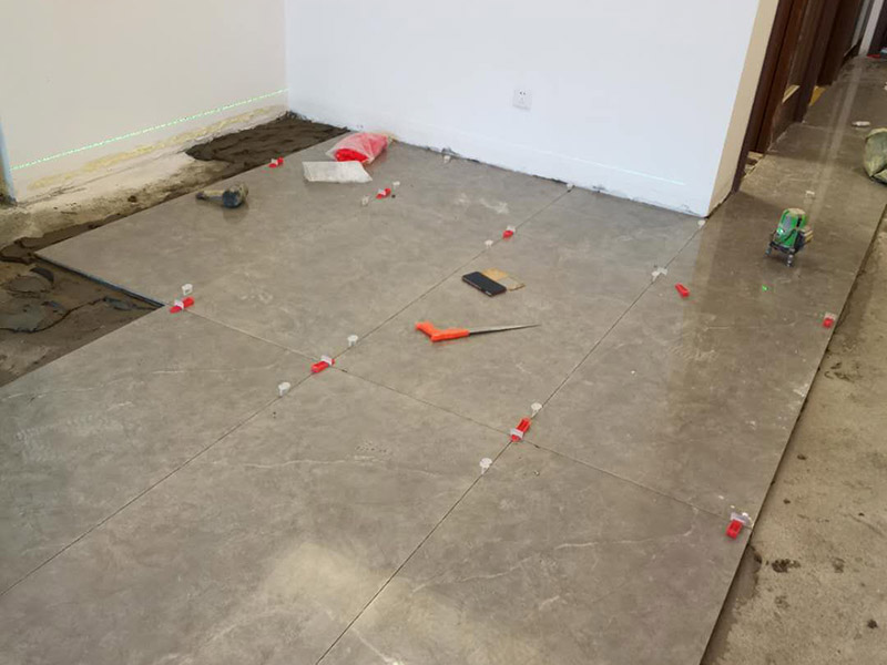 客廳地磚鋪貼：地磚鋪貼前，應(yīng)將地面清掃干凈，尤其是凝結(jié)后的混凝土，否則，地磚鋪貼后會(huì)出現(xiàn)翹邊、空鼓等現(xiàn)象，然后再灑水潤(rùn)濕地面。地面充分濕潤(rùn)，但不能有積水，然后將3:1混合好的沙子水泥鋪在地面上，進(jìn)行基層處理。在地磚背面均勻抹水泥砂漿作為粘合層，厚度不低于1cm，然后鋪在剛才試鋪的位置上，用橡皮錘輕敲地磚飾面直至密實(shí)平整達(dá)到要求。地磚鋪完后24h進(jìn)行清理勾縫，勾縫前應(yīng)先將地磚縫隙內(nèi)雜質(zhì)擦凈，用專(zhuān)用填縫劑勾縫，完工后（一般宜在24h之后）再用棉紗等物對(duì)地磚表面進(jìn)行清理。