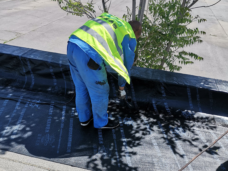 屋頂防水卷材鋪貼:清除基層表面雜物、油污、砂子，凸出表面的石子、砂漿疙瘩等應(yīng)清理干凈，清掃工作必須在施工中隨時(shí)進(jìn)行，并修補(bǔ)平整表面。尤其鏟除排水口、煙囪、管壁上的水泥砂漿等附著物；根據(jù)施工現(xiàn)場(chǎng)狀況，進(jìn)行合理定位，確定卷材鋪貼方向，在基層上彈好卷材控制線，依循流水方向從低往高進(jìn)行卷材試鋪。卷材試鋪后，先將要鋪貼的卷材剪好，反鋪于基面上(即是底部隔離紙朝上)，撕剝?nèi)ゾ聿母綦x紙。撕剝時(shí)，已剝開(kāi)的隔離紙宜與粘結(jié)面保持45～60度的銳角，防止拉斷隔離紙，盡量保持在自然松弛狀態(tài)，但不要有皺折。