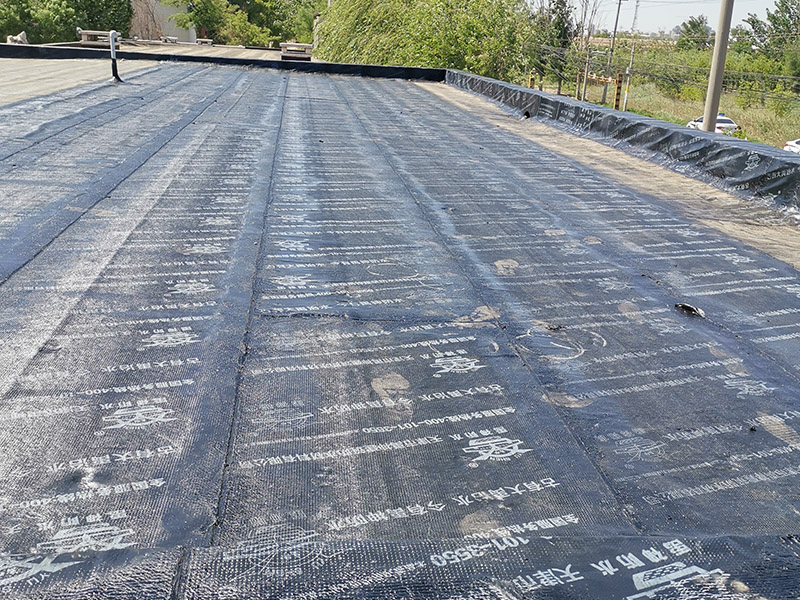 屋頂防水卷材鋪貼:清除基層表面雜物、油污、砂子，凸出表面的石子、砂漿疙瘩等應(yīng)清理干凈，清掃工作必須在施工中隨時(shí)進(jìn)行，并修補(bǔ)平整表面。尤其鏟除排水口、煙囪、管壁上的水泥砂漿等附著物；根據(jù)施工現(xiàn)場(chǎng)狀況，進(jìn)行合理定位，確定卷材鋪貼方向，在基層上彈好卷材控制線，依循流水方向從低往高進(jìn)行卷材試鋪。卷材試鋪后，先將要鋪貼的卷材剪好，反鋪于基面上(即是底部隔離紙朝上)，撕剝?nèi)ゾ聿母綦x紙。撕剝時(shí)，已剝開(kāi)的隔離紙宜與粘結(jié)面保持45～60度的銳角，防止拉斷隔離紙，盡量保持在自然松弛狀態(tài)，但不要有皺折。