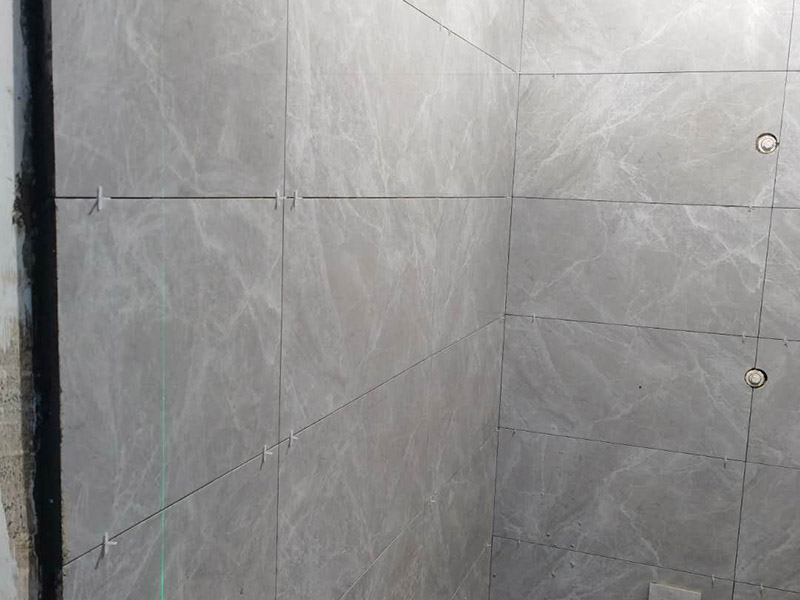 衛(wèi)生間貼磚施工：應(yīng)全部清理墻面上的各類污物，打掃干凈現(xiàn)場(chǎng)，特別是腳落里。用泥刀先批墻，后用水泥漿找平。這個(gè)工序很重要，確保底子平，防止貼后空鼓。墻面要刷防水涂料，防止貼后浸水，一般高度不低于1.8米，刷的時(shí)候會(huì)稍高一些。根據(jù)設(shè)計(jì)鋪貼圖樣的要求，確定排磚方案，用墨斗彈線，以減少施工損耗。把剛剛攪拌好的粘結(jié)劑漿料均勻的刮到墻上。瓷磚上墻將經(jīng)過(guò)預(yù)先清潔的瓷磚平整地鋪貼在粘結(jié)劑漿料基層上，使用橡膠錘將瓷磚拍實(shí)鋪平。施工過(guò)程中，可小幅度轉(zhuǎn)動(dòng)瓷磚，使?jié){料與瓷磚背面充分接觸。專家建議在鋪貼時(shí)，隨機(jī)取下已鋪貼于基層上的瓷磚作檢查。確保漿料與瓷磚背面的充分接觸。 留縫大小調(diào)整根據(jù)瓷磚的尺寸，在磚與磚之間預(yù)留相應(yīng)尺寸的縫隙留待嵌縫。可用牙簽等先固定，粘結(jié)劑具有一定的可調(diào)整性，可對(duì)留縫的大小進(jìn)行調(diào)整。