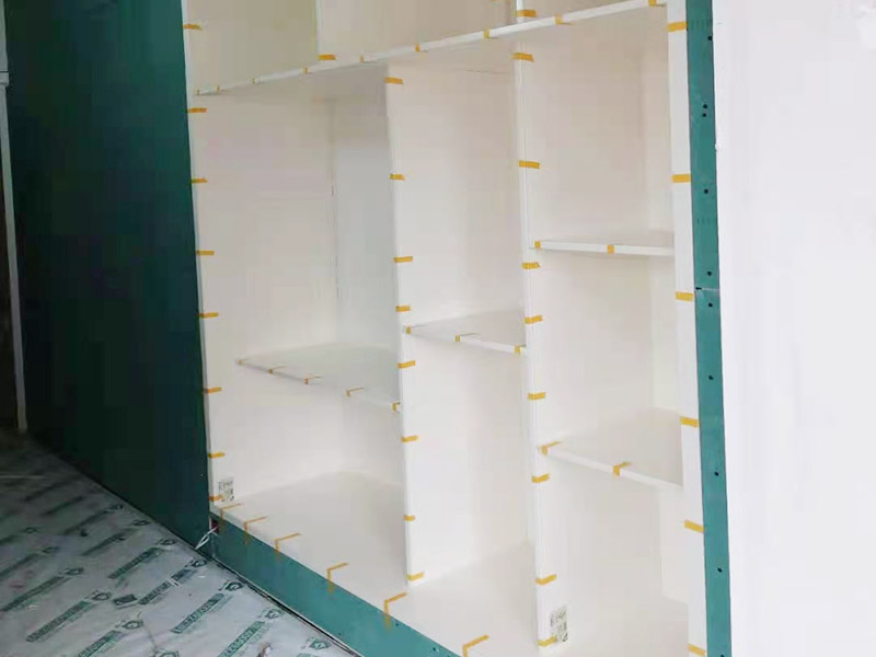 客廳定制柜體安裝：用墊布點(diǎn)好地板，先從靠墻的一端寬側(cè)板開始組裝，將寬側(cè)板平放于地面上（離后墻面保持700mm間隔）。首先將填好的三合一膠塞的板件，平放在墊布上，檢查孔距與圖紙相符，并裝上三合一單連桿。然后將固層釘上木塞，固定于寬側(cè)板上面，頂板大柄孔朝上，其余固層都朝下，腳線大柄孔朝內(nèi)（中間固層與L架高度一致，即底板到固層內(nèi)空為960mm，現(xiàn)場(chǎng)打?qū)影蹇祝?。放上?cè)板，釘上木塞，木塞要求連通兩邊的固層。在第二個(gè)柜固層上面裝好雙連桿，留意雙連桿上面大柄只能鎖住一半，即90&deg;。當(dāng)兩件固層與側(cè)板固定后再同時(shí)擰緊大柄。裝第三個(gè)柜時(shí)重復(fù)第二個(gè)柜的安裝步驟。