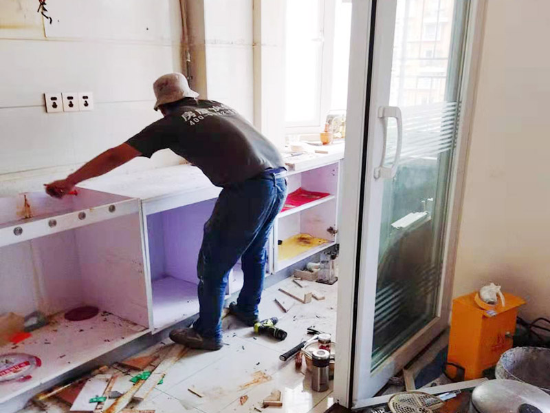 廚房櫥柜安裝：清理：對廚房作防護(hù)措施，掛擋布、廚房墻面等做簡單清理，以便準(zhǔn)確測量地面水平。櫥柜安裝一般先從地柜開始。把櫥柜外包裝拆開后。在櫥柜的邊緣貼上防火膜封邊。在下柜底部安裝上支腳，根據(jù)地面水平高度調(diào)整櫥柜。 櫥柜安裝需要找出基準(zhǔn)點(diǎn)，L型廚房從直角處向兩邊延伸，U型廚房則先將中間的一字型柜體放整齊后，再從兩個(gè)直角處向兩邊站看，這樣可以避免出現(xiàn)縫隙。櫥柜框架安裝牢固定位后，需要在櫥柜背面安裝背板。一般安裝下水都會現(xiàn)場開孔，工人會用專業(yè)的打孔器按照管道大小進(jìn)行打孔，打孔的直徑應(yīng)比管道大3-4毫米，并且打孔后要將開孔部分用密封條封邊，防止邊緣滲水木材變形。